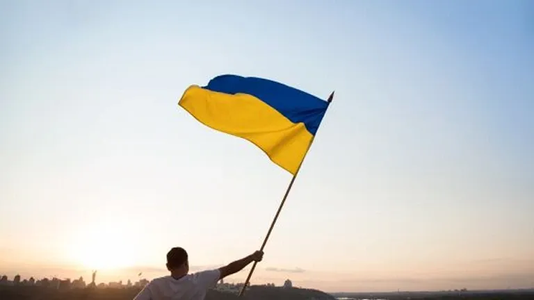 Людина тримає прапор України на фоні неба